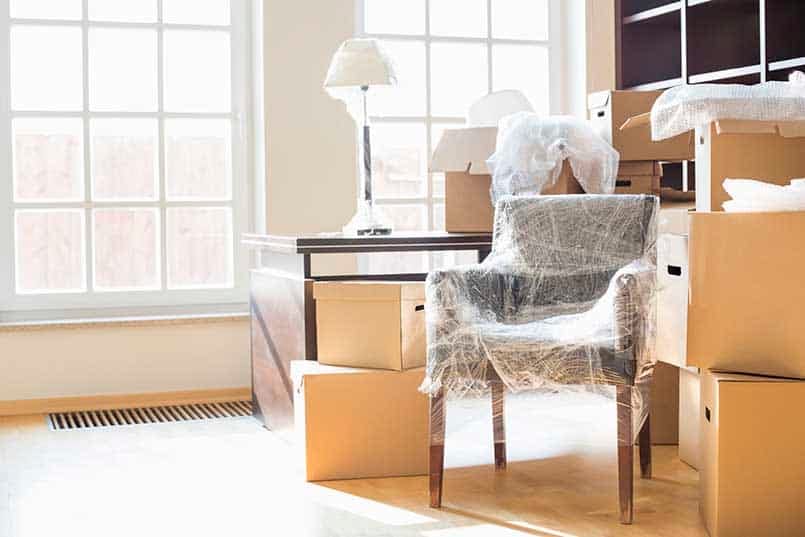 Furniture wrapped in protective plastic beside packed moving boxes in a bright living room